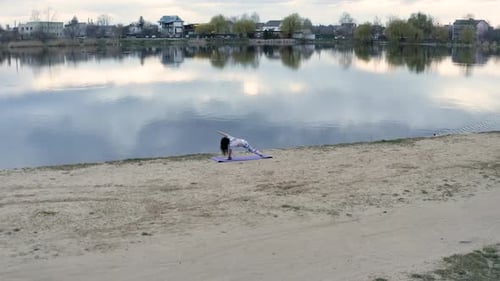 Woman Practices Yoga by Calm Lake on Beach