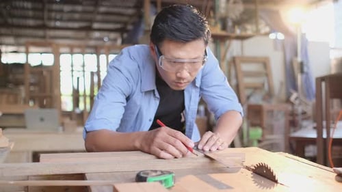 Man Measures Wood at Workbench in Woodshop