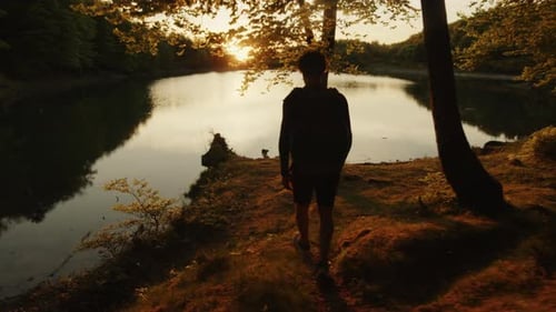 Boy with Backpack Walks Near the Lake in the Mountains