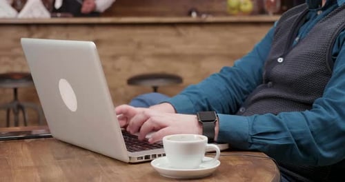 Detailaufnahme von männlichen Händen, die einen Text auf seinem Laptop tippen und Kaffee trinken