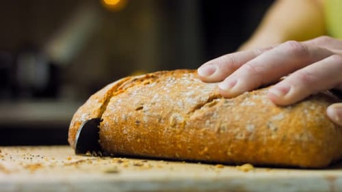 Hands Slice Fresh Loaf of Bread on Board