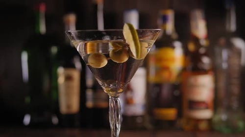 Closeup of a Martini Glass with Olives and Lemon Slowly Rotating on the Bar