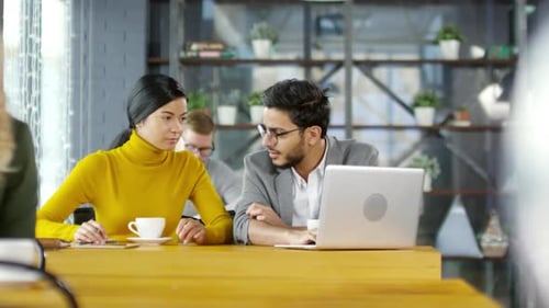 Young Diverse Colleagues Discussing Project on Laptop in Cafe
