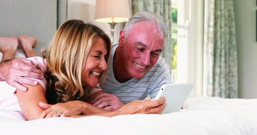 Happy Senior Couple Using Tablet in Bed