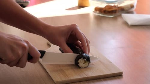 Hands Slicing Sushi Roll on Cutting Board