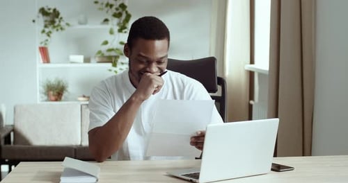 Young Man Reads Letter with Smile at Desk