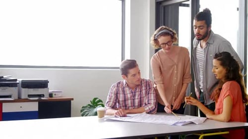 Team Discussing Blueprint Around Table in Bright Office