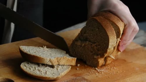 Hands Slice Loaf of Bread on Cutting Board