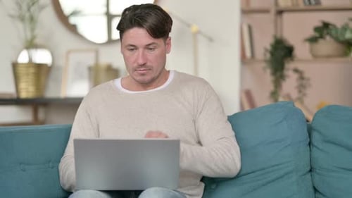 Man Closing Laptop on Couch Indoors During Day