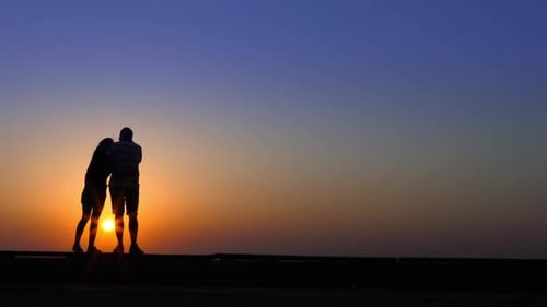 Couple Embracing at Sunset Silhouetted on Horizon