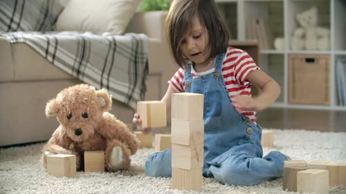 Little Girl Plays with Wooden Blocks in Home