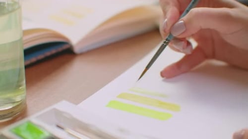 A Young Woman with a Brush and Paints Chooses a Suitable Shade for the Logo Design or Walls