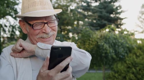 Happy Senior Man Chatting on Phone's Web Camera He Has Joy and Gestures in Park