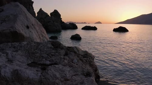 Entspannende Meereswellen und riesige Felsen am tropischen Strand bei Sonnenuntergang