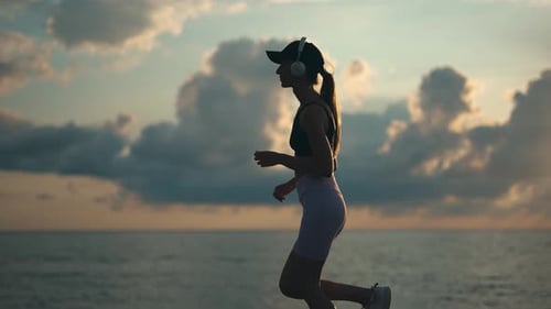 A Young Woman Runner is Listening to Music in Earphones and Training By a Sea