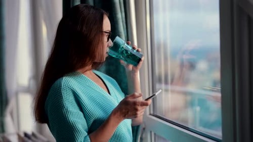 Woman Using Mobile Phone and Drinking Water Indoors