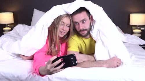 Paar auf einem bequemen Bett beim Selfie