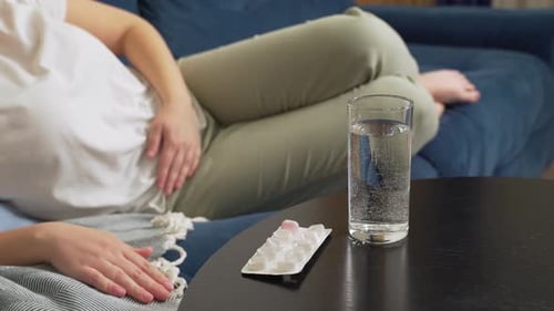Woman Lying on Couch with Pills and Water