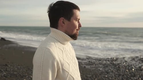 Young Man Is Standing Alone on the Beach During Wintertime and Watching the Sea.
