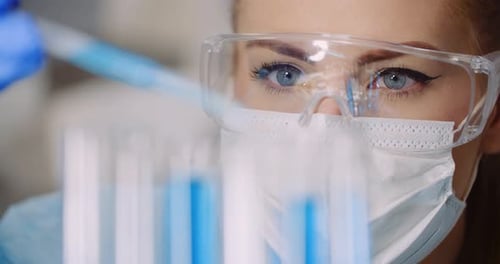 Woman Adds Liquid to Test Tubes in Lab