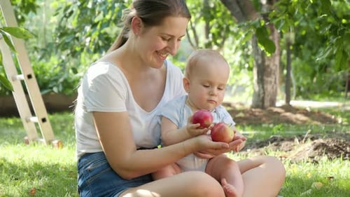 Cute Smiling Baby Boy with Mother Holding Red Ripe Apples at Orchard