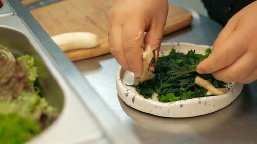 chef puts pieces of banana on leaves of nettle for salad in a restaurant kitchen. cooking salad step
