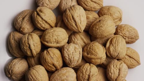 Cinematic, rotating shot of walnuts in their shells on a white surface - WALNUTS