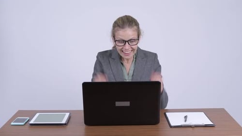 Junge glückliche blonde Geschäftsfrau benutzt Laptop und bekommt gute Nachrichten bei der Arbeit