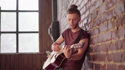 Young Man Playing Guitar Against Brick Wall