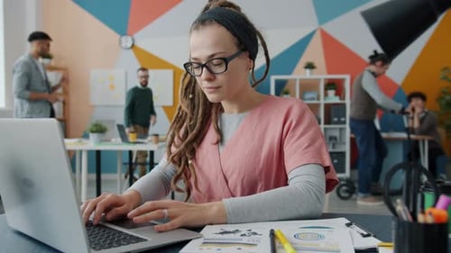 Slow Motion of Young Woman Using Computer While Colleagues Working and Having Fun in Office