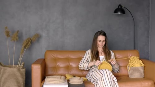 Woman Crocheting a Yellow Bag on a Brown Couch