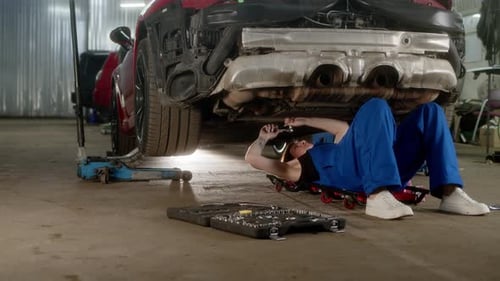 Uma funcionária do serviço de automóveis se deita embaixo do carro e o conserta
