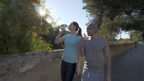 Athletic Couple Walks and Hydrates in Urban Park