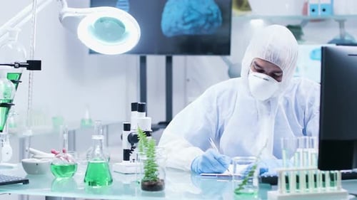 In High-end Biochemistry Laboratory a Scientist in Coveralls Is Making Notes