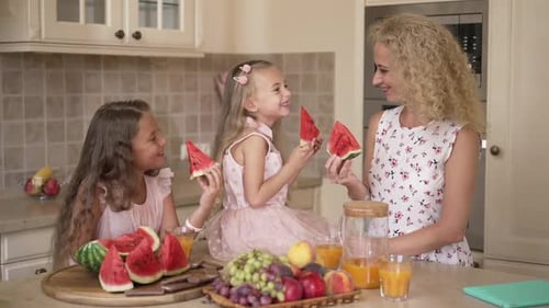 Mother and Two Daughters Enjoying Watermelon in Kitchen