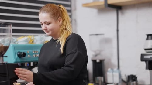 Positive Young Caucasian Woman Making Hot Drink in Coffee Maker Looking at Camera and Smiling