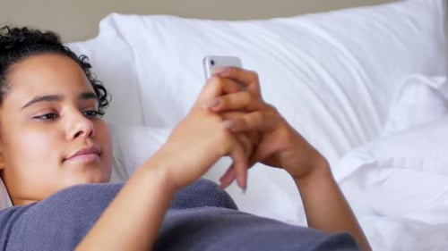 Woman Relaxes in Bed with Smartphone