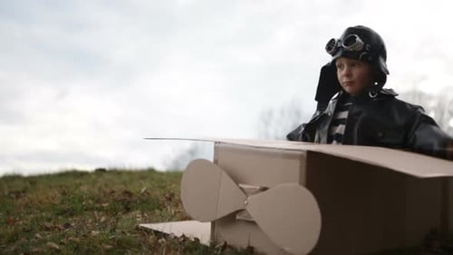 Junger Pilot oder Fliegerjunge spielt und lächelt mit seinem Carboard-Flugzeug Nahaufnahme