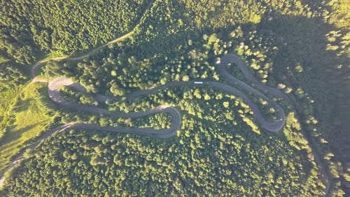 Aerial view of winding road with mowing cars and trucks in high mountain pass trough dense woods.