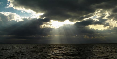 Dramatic Sunlight Breaks Through Clouds Over Dark Ocean