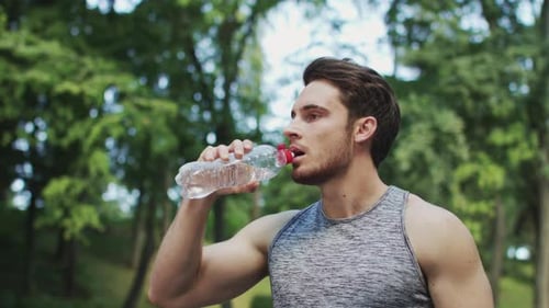 Sport Man Drinking Water From Bottle After Running Exercise in Summer Park
