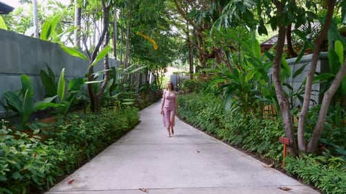 Young Beautiful Woman Walking Among Green Tropical Trees at a Luxury Hotel Area