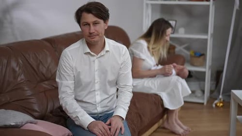 Père heureux et reconnaissant mari admirant une femme et un fils nouveau-né assis à l'arrière-plan se tournant vers la caméra