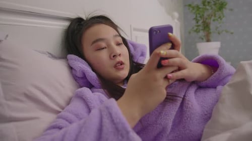 Young Woman Using Phone Lying in Bed