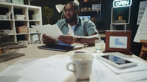 Focused African American Businessman Reading Business Report in Late Office.