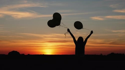 Silhouette Person with Balloons in Sunset Field