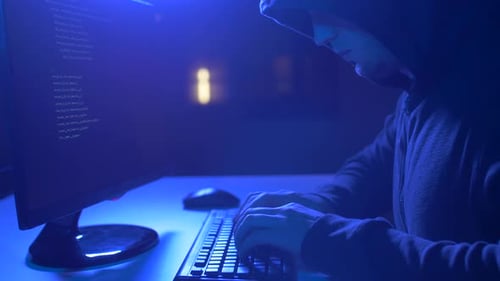 Hooded Hacker Typing Code on Computer at Night