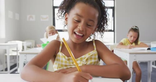 Video of happy biracial girl sitting at school desk and learning