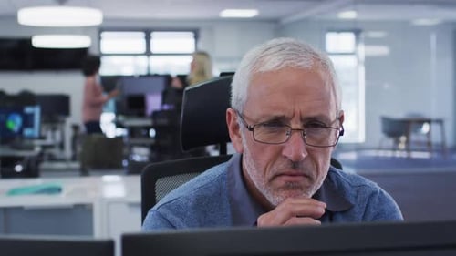 Nachdenklicher Mann schaut auf seinen Computerbildschirm, während er im Büro auf seinem Schreibtisch sitzt