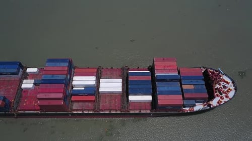 Luftseite und Draufsicht eines großen Containerschiffs, das an einem sonnigen Tag langsam entlang fährt.